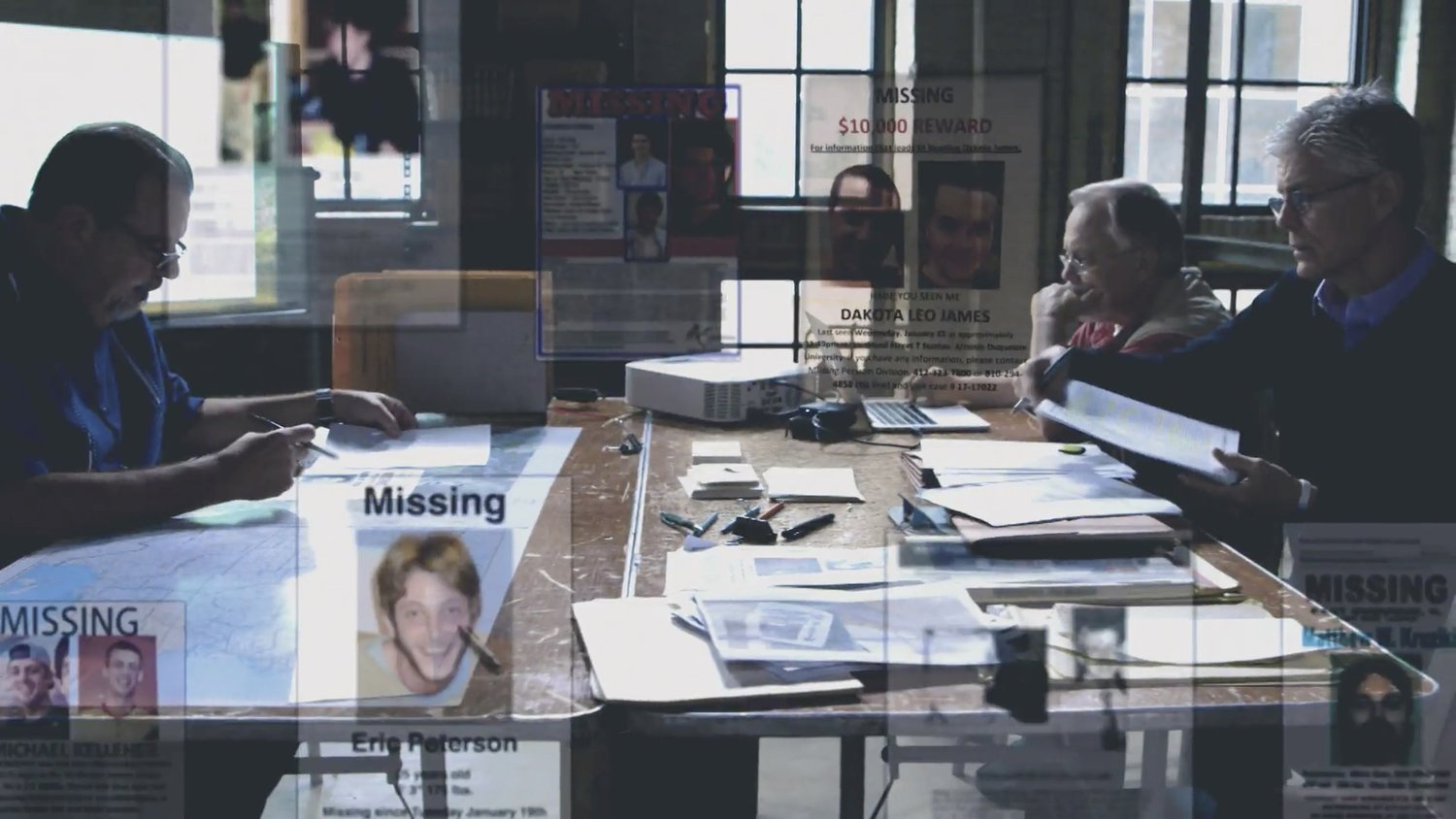 Investigators reviewing missing persons case files and evidence around a conference table
