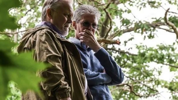 Two investigators standing together among trees reviewing a case